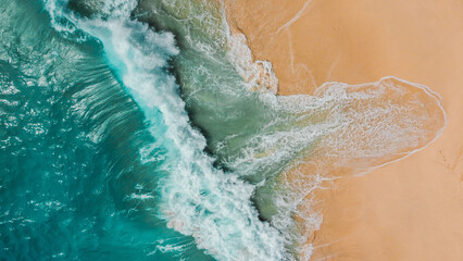 A breathtaking aerial view of turquoise waves gently crashing onto a golden sandy beach, showcasing the dynamic interaction between the ocean and shoreline.
