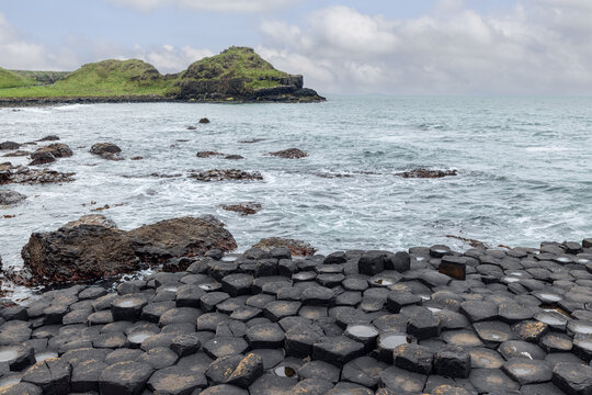 Basalt hexagonal columns of Giant's Causeway meet the Atlantic Ocean in Northern Ireland, with rocky shorelines and green hills in the background