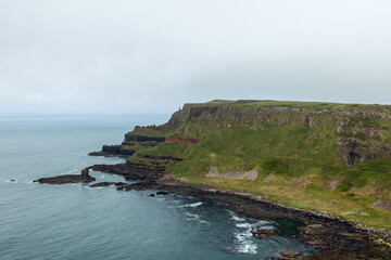 Giant Causeway coastal cliffs, with striking layers of basalt rock and green hills, meet the...