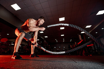 Man workouts with battle ropes in gym. A fitness enthusiast demonstrates strength and agility while...