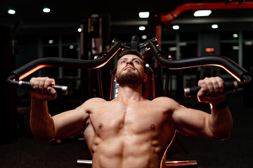 Man exercising in a gym with dim lighting at night. A man lifts weights on a machine in a dimly lit...