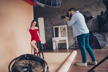 Photo of excited cameraman capturing video of shiny cute girl dressed red look indoors workplace studio