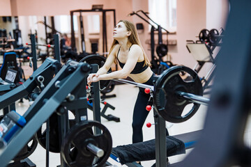 Young woman resting between exercises at the gym. A young woman takes a break from her workout, reflecting on her routine in a modern gym filled with equipment.