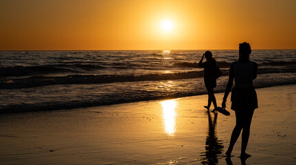 Two women walking on the beach during sunset © Raquel