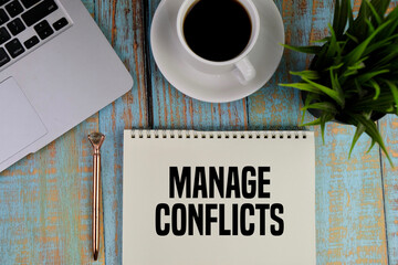 A notebook with the words MANAGE CONFLICTS on grey background with mobile phone, pen and...