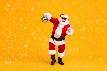 Full body photo crazy santa claus with grey beard hold disco ball show horns symbol dance x-mas christmas party wear sunglass headwear cap isolated bright shine color background