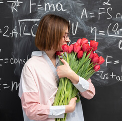 A young attractive teacher stands with a bouquet of flowers in the classroom. Teachers day and graduation concept