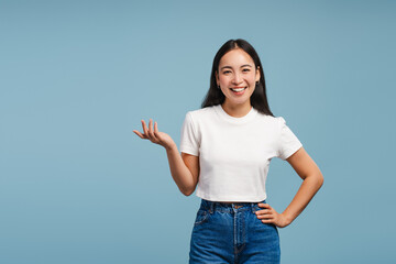 Smiling, attractive Asian woman showing something with hand, explaining isolated on blue background
