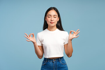 Young Asian woman meditating with closed eyes isolated on blue background, harmony concept