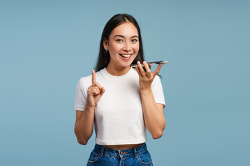 Attractive Asian woman talking on speakerphone and pointing index finger looking at camera