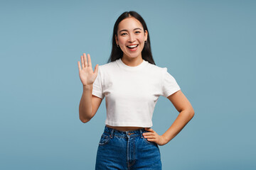 Smiling, Asian woman waving and smiling standing isolated on blue background