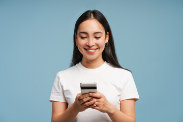 Fototapeta premium Young, smiling Asian woman using smartphone and smiling on blue background