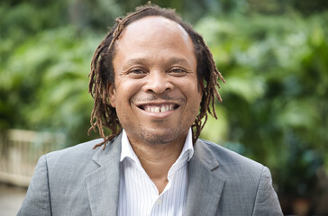 Happy, smiling, positive and friendly middle aged African office worker or businessman in green park near office