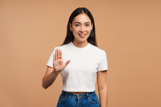 Young, beautiful Asian woman smiling and showing stop gesture with hand on beige background - Powered by Adobe