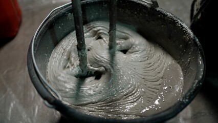 Construction worker mixing cement in bucket with electric mixer