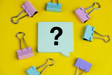 Question mark speech bubble isolated on yellow background surrounded by colorful paper clip. 