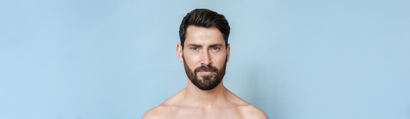 Closeup headshot portrait of mature smiling handsome bare shoulders man having beard, perfect skin looking at camera isolated over blue background. Masculine, healthcare, bodycare. Banner, copy space