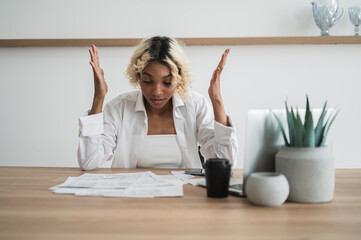 Broke,Frustrated african american girl sitting in fronu of pile of bills and invoices.Expenses,cost...