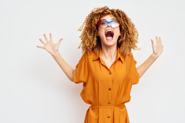 Happy woman with curly hair expressing excitement, wearing colorful sunglasses and an orange shirt against a minimalist light background Energetic and vibrant concept