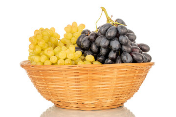 Two bunches of ripe white and black grapes in a straw bowl, macro, isolated on white background.