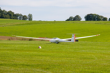 Fototapeta premium a white glider landing on a green meadow with flaps up 