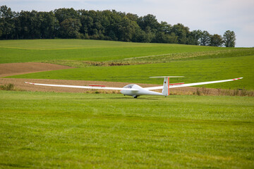 Fototapeta premium a white glider landing on a green meadow with flaps up 