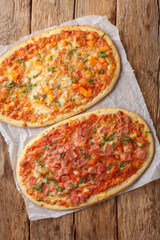 Roman pizzas three cheeses and cheese with jamon close-up on parchment on wooden table. Vertical top view from above