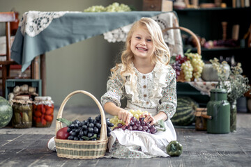 A little toddler girl with long blond hair holding a large bunch of grapes in her hands.