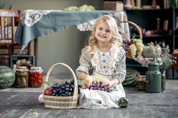 A little toddler girl with long blond hair holding a large bunch of grapes in her hands.