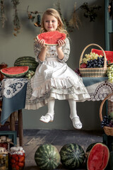 Little girl with long blond hair eats watermelon in the village