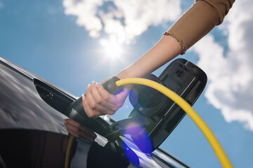 Woman opening an electric car charging socket cap and plugging in a charger