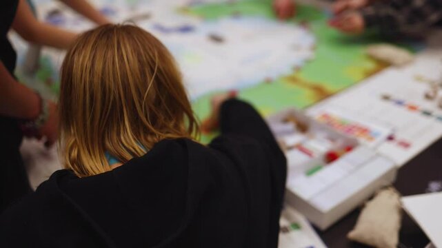 Process of playing tabletop board game on the table, fun with friends and family in room indoors, board game concept, company group of students adults play board games, roll the dice on a game map