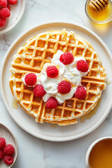 plate of waffles with the top drizzled in cream and garnished with raspberries, placed on an off-white marble surface, surrounded by small bowls filled with honey 