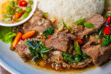 Closeup Stir-fried beef with basil in a blue plate with fish sauce, chili, cucumber and lettuce on a wooden table.