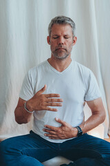 A man sitting in lotus position, practicing alternate nostril breathing exercises during a...
