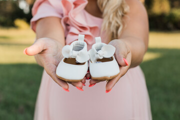 pregnant woman holding a pair of cute leather baby shoes with bows in her hands 