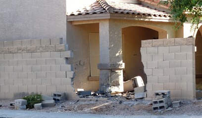 A damaged brick wall and cracked columns frame a home's entrance after an impact. Debris scatters across the yard, telling the story of an unfortunate event that has left its mark on the property.
