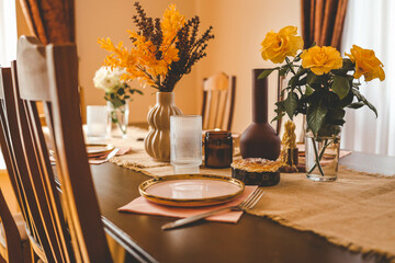 Beautiful table setting with a ceramic pink plate, a fork, and a glass of water on a rustic burlap tablecloth. Yellow roses, decorative vase, and pastry in background create a cozy, warm atmosphere