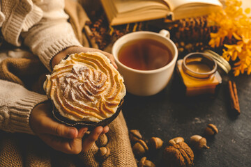 Girl holding a powdered cinnamon bun in cozy autumnal setting with acorns, candles, and dried...