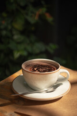 Coffee with hot chocolate in a beige cup, surrounded by green plants