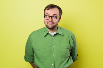 Fototapeta premium Casual portrait of a man wearing glasses and a green shirt, standing against a vibrant yellow background, showcasing a playful and thoughtful expression in a colorful setting.