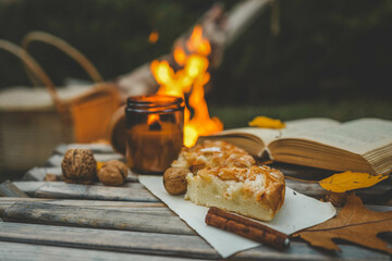 Rustic autumn scene with a piece of apple pie, walnuts, and cinnamon sticks on a wooden table near...