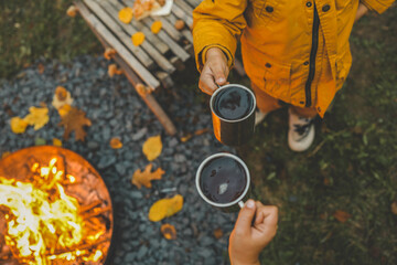 Children in warm clothing holding cups of hot drink near a bonfire in the evening. Cozy autumn outdoor scene with a fire pit, fallen leaves, and rustic snacks, capturing the essence of fall warmth