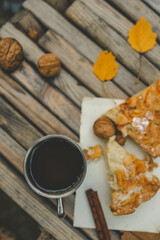 Cozy autumn picnic setup with a metal mug of hot tea, a piece of pie, walnuts, and cinnamon sticks on a rustic wooden table