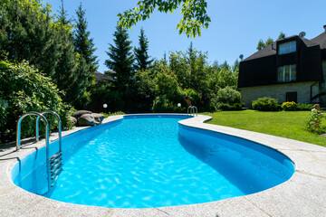 A magnificent swimming pool on the lawn of a private house on a clear sunny day. Dense .greenery surrounds the courtyard.