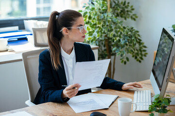 Business woman working with computer while consulting some invoices and documents at the office