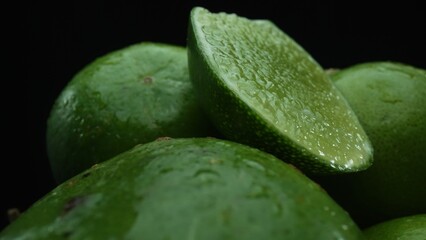 Slices of lime are meticulously arranged in a pile, set against a black background. Each lime slice is captured in stunning detail, its vibrant green hue and enticing texture. Close up. Comestible.