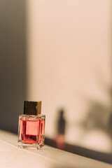 glass perfume bottle with gold cap in pink shade on textured surface, with soft shadow in warm, ambient lighting