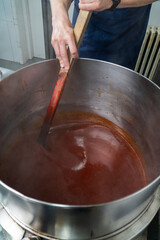Stirring Rosehip Jam in Artisan Factory.  The large stainless-steel pot holds the simmering jam, with a spatula gently stirring the thick mixture. 