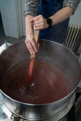 Stirring Rosehip Jam in Artisan Factory.  The large stainless-steel pot holds the simmering jam, with a spatula gently stirring the thick mixture. 